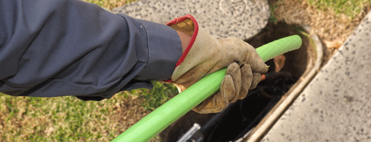 Gloved hand pulling a thick green cable from a small ground opening.